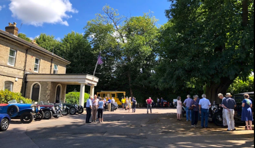 Large building exterior with vintage cars and many viewing