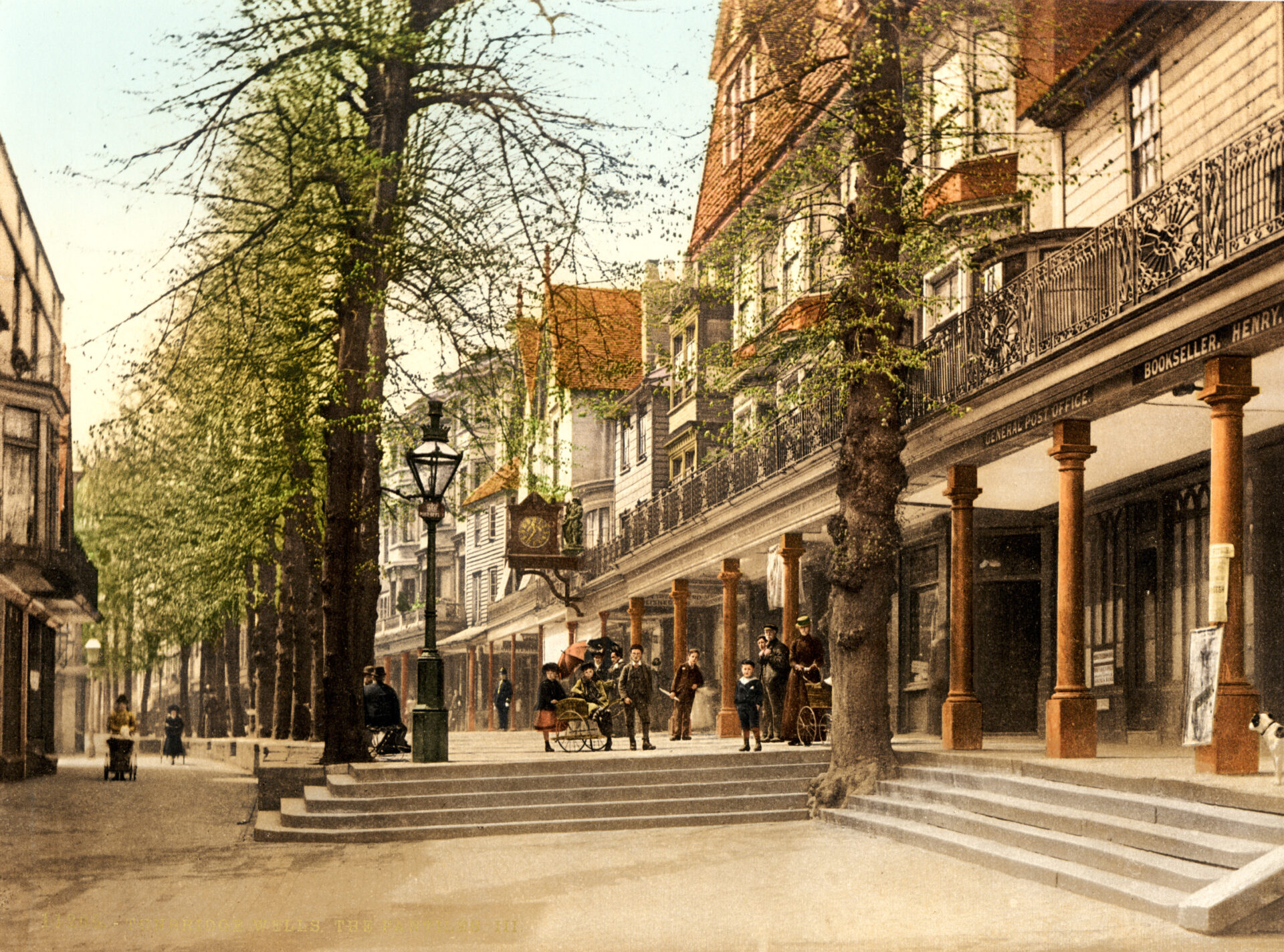 Scene from 1895 - Sweeping Victorian shops and apartment above with a collonade front, tree lined walkways, and steps. Poeple include policeman, woman pushing pram, and a man pulling a single sseater carriage on two wheels.