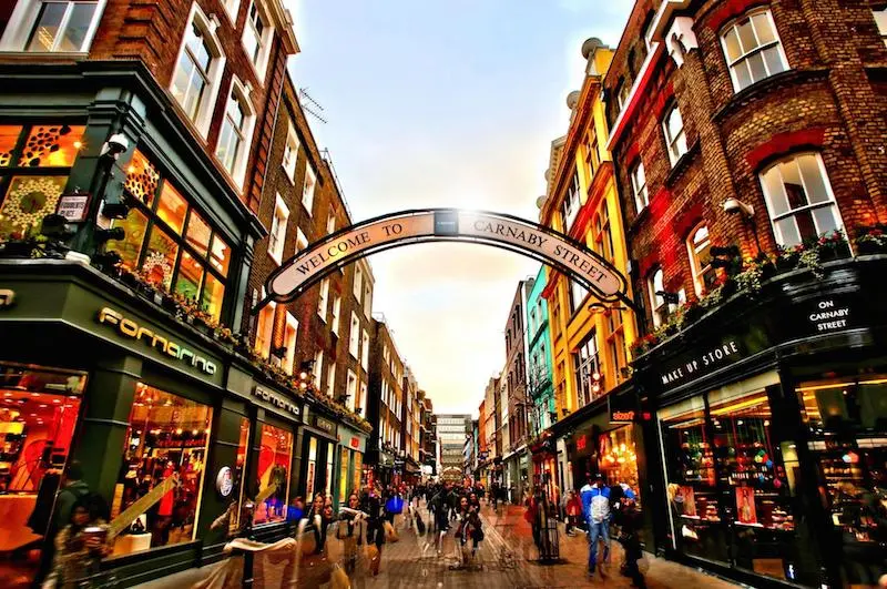 Evening view down Carnaby Street showing Welcome to Carnaby Street arch sign with shops windows illuminated and pedestrians ghosted through photo timing