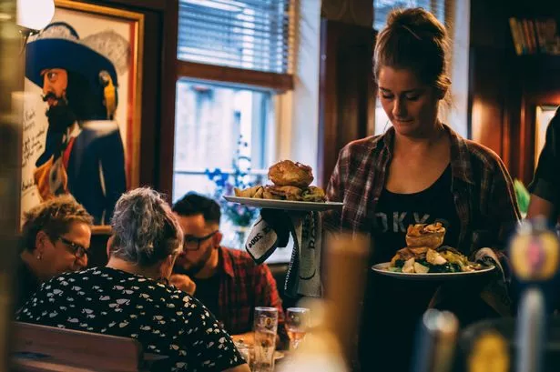Waitress bringing two raost dinners with large yorkshires to a table in a pub